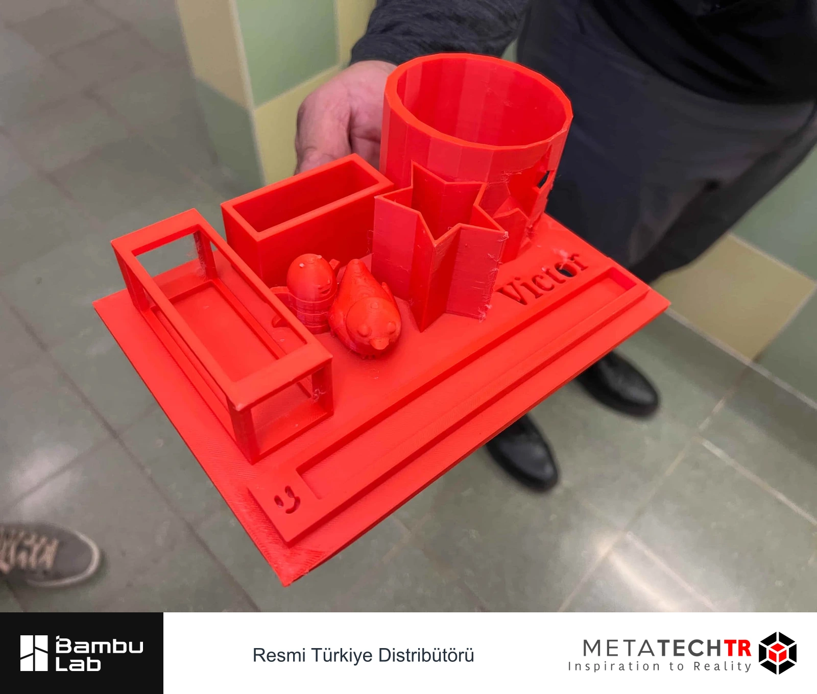 Farklı bölmeleri ve Victor yazısı bulunan kırmızı 3D baskılı masa düzenleyici.