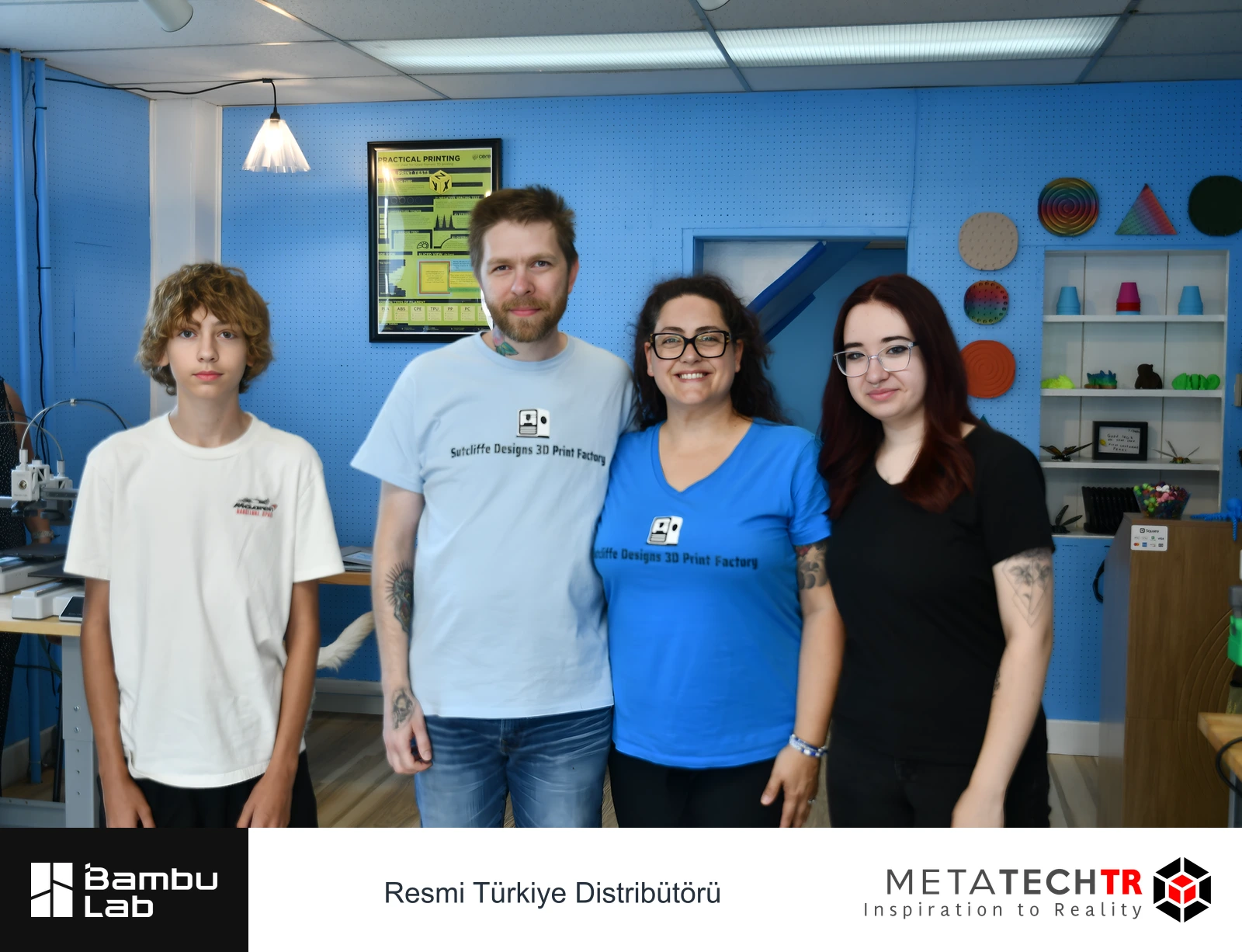 Basılı örneklerin sergilendiği mavi duvarın önünde Sutcliffe Designs ekibinin grup fotoğrafı.